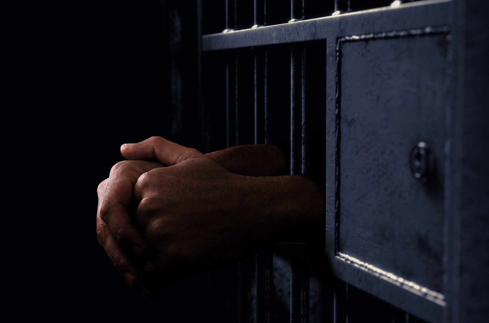 A closeup of a dimly lit prison holding cell door with a pair of hands reaching out
